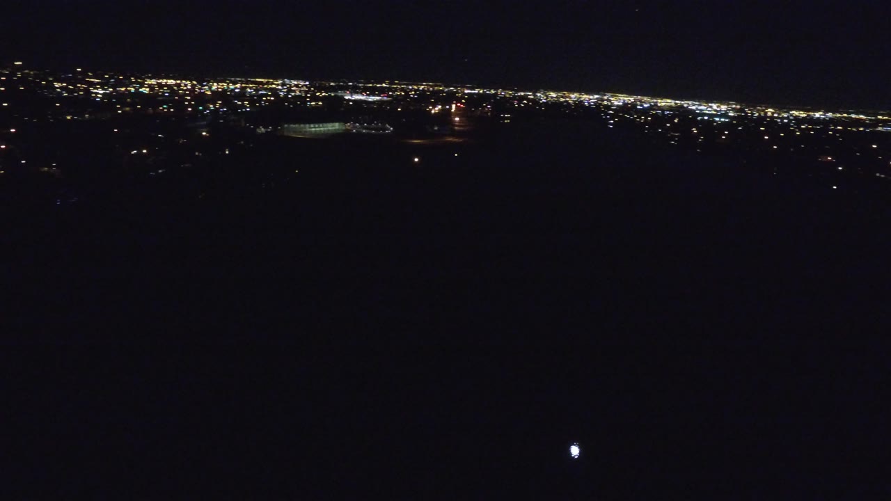 Denver city lights continue across the horizon from a high nighttime aerial view, with a small bright point low in the frame and no visible people.