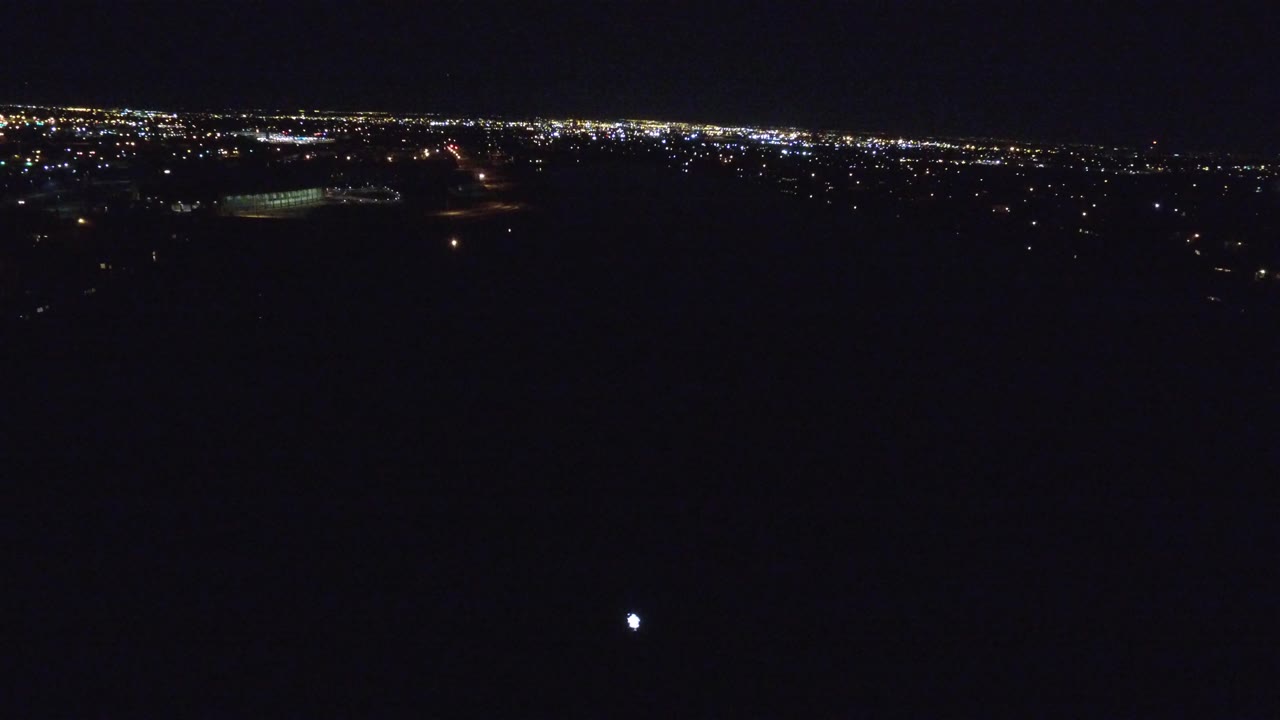 Denver, Colorado at night from above, with a thin band of city lights across the horizon, a dark foreground, and no visible people.