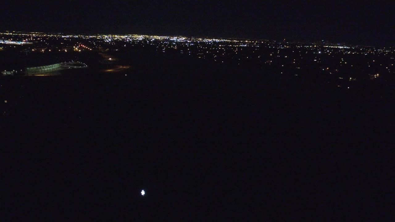 Distant city lights over a dark foreground at night.