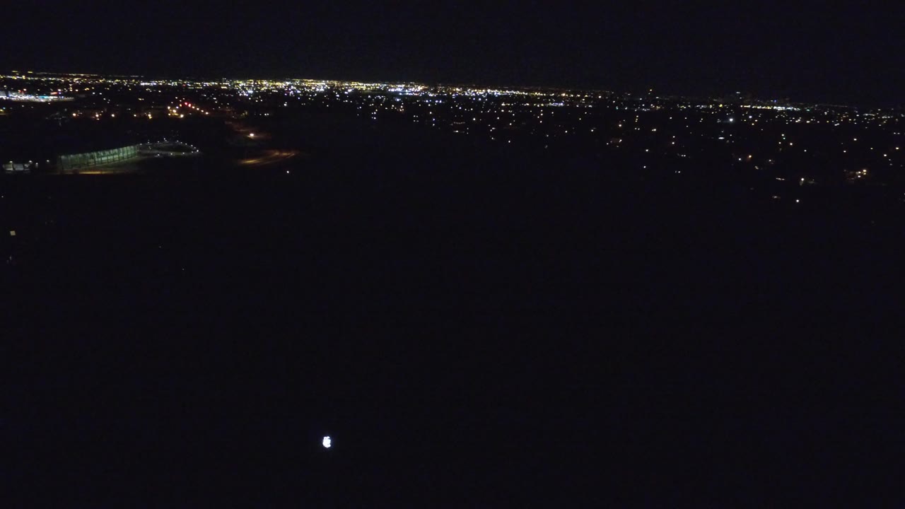 Denver night horizon with clustered lights in the distance, a small bright point in the dark foreground, and no visible people.