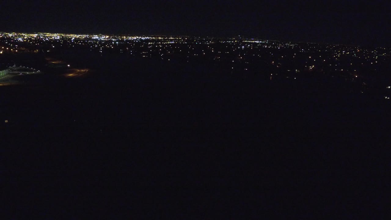 Dark aerial view with distant city lights on the horizon.