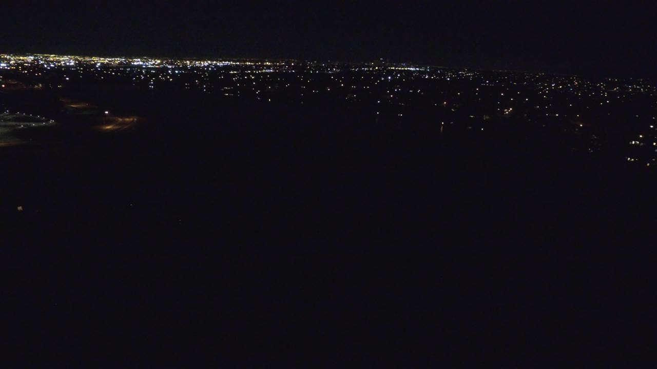 Dark elevated city view with scattered lights and a bright horizon.