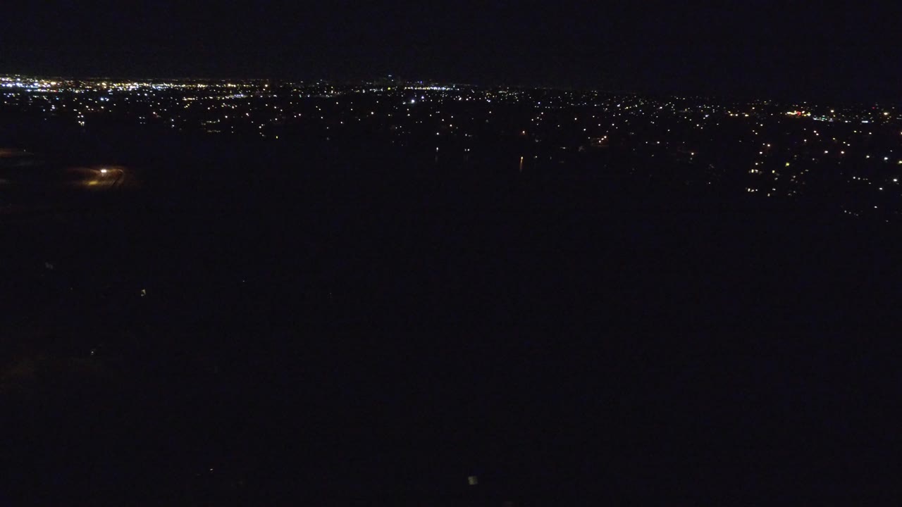 Denver, Colorado night aerial frame showing a mostly black foreground, scattered city lights on the horizon, a few amber lights below, and no visible people.