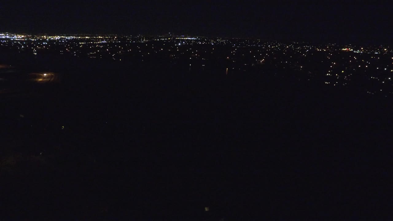 Denver, Colorado aerial view at night with a broad dark foreground, a thin band of urban lights in the distance, and no visible people.