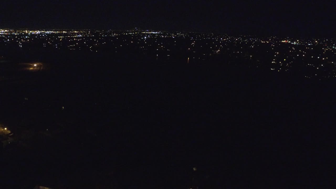 Dark aerial cityscape with brighter lights clustered near the horizon.