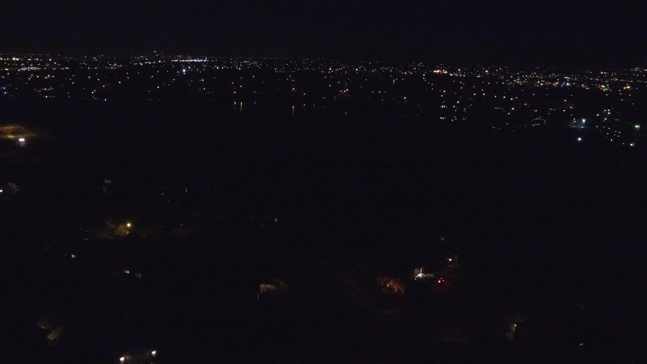 Dark aerial city view with scattered lights along a distant horizon.