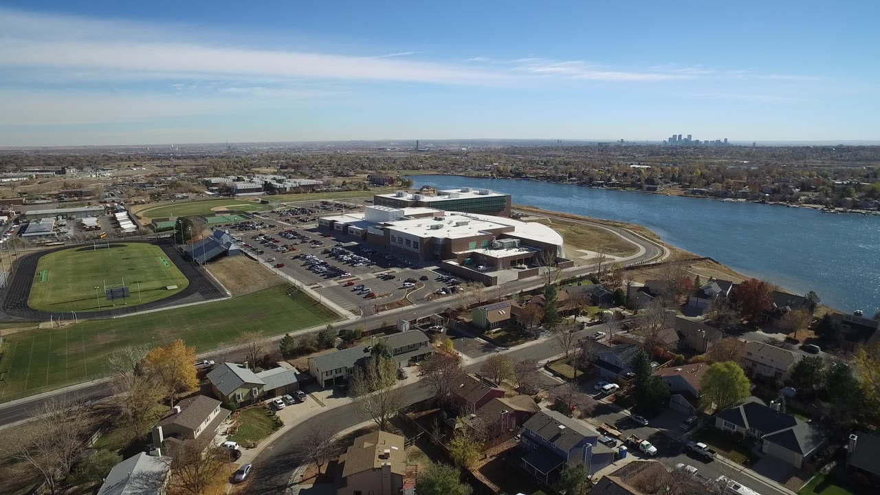 Drone-height view of a suburban riverfront with fields, roads, buildings, and homes.