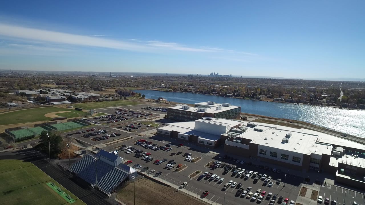 At 0:01, the drone view holds over Westminster parking lots, office or industrial buildings, sports fields, reflective river water, blue sky, and no visible people.