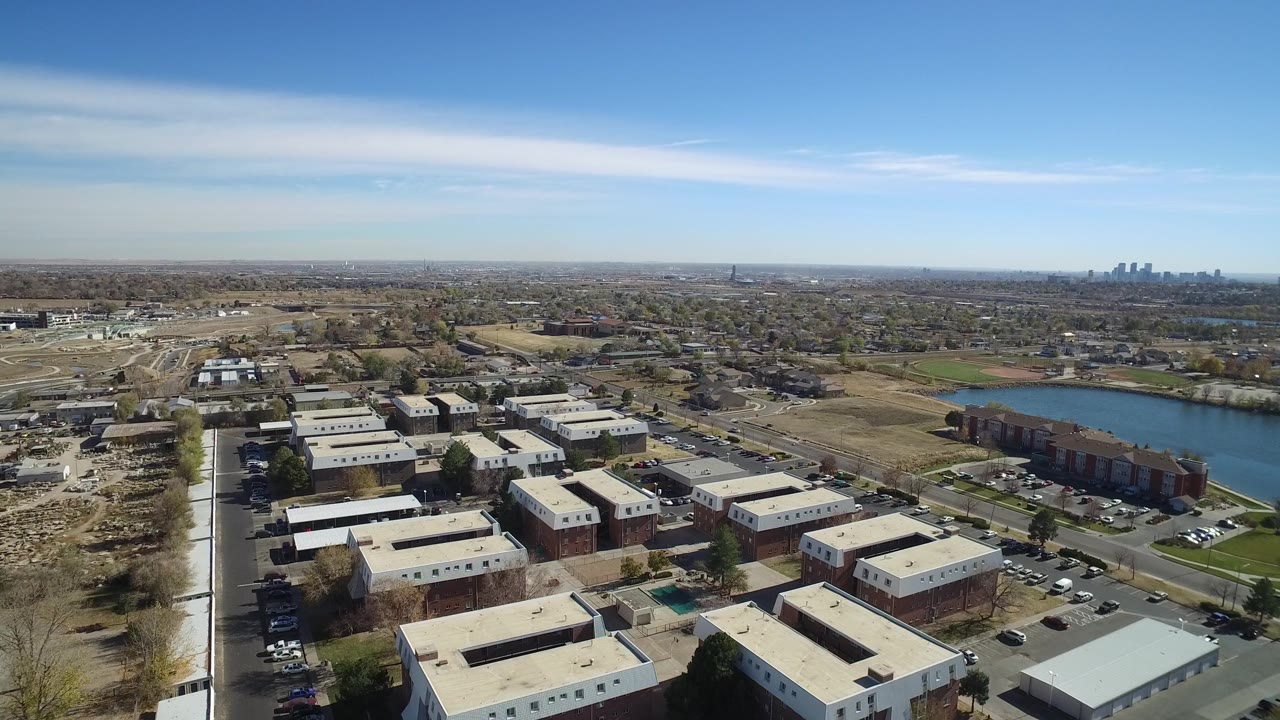 Drone-height view across rooftops and roads toward lake water and a distant skyline.