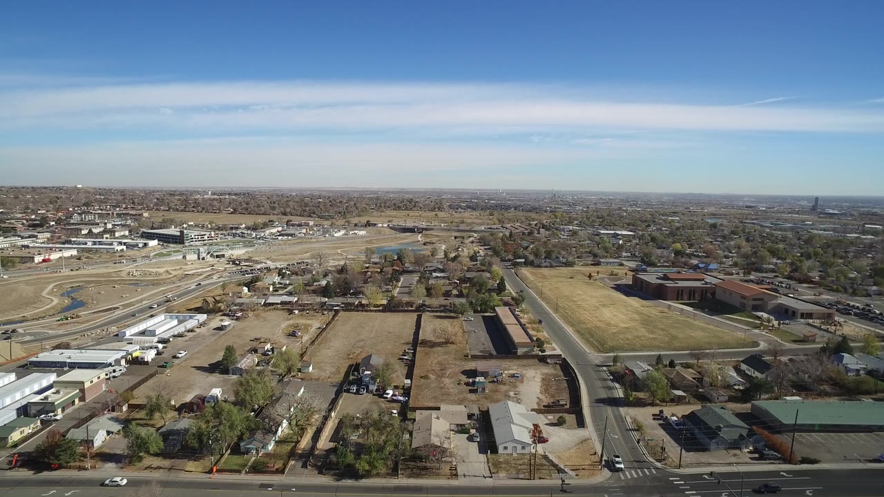 Second aerial frame of Westminster, Colorado, with the road intersection lower in frame, parking areas and low commercial roofs closer to view, and no visible people.