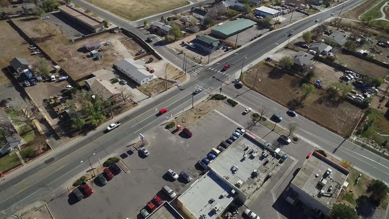 Overhead Westminster, Colorado frame with the main road crossing diagonally, parking lots in the lower foreground, homes beyond the intersection, and no visible people.