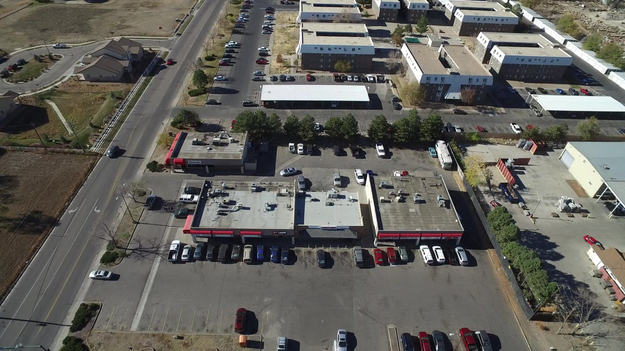 High overhead frame of Westminster, Colorado commercial parking lots, low industrial buildings, a vertical road, dry lots, parked cars, and no visible people.