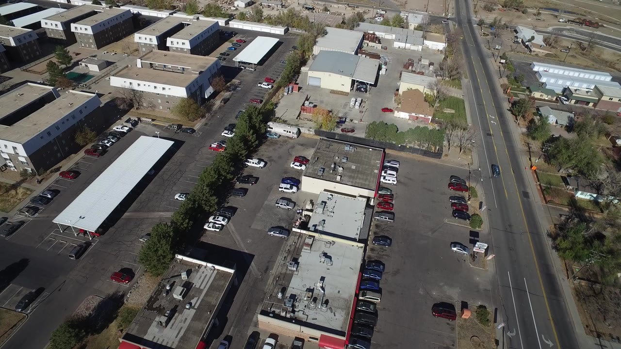 Overhead view of a parking lot beside a road and commercial buildings.