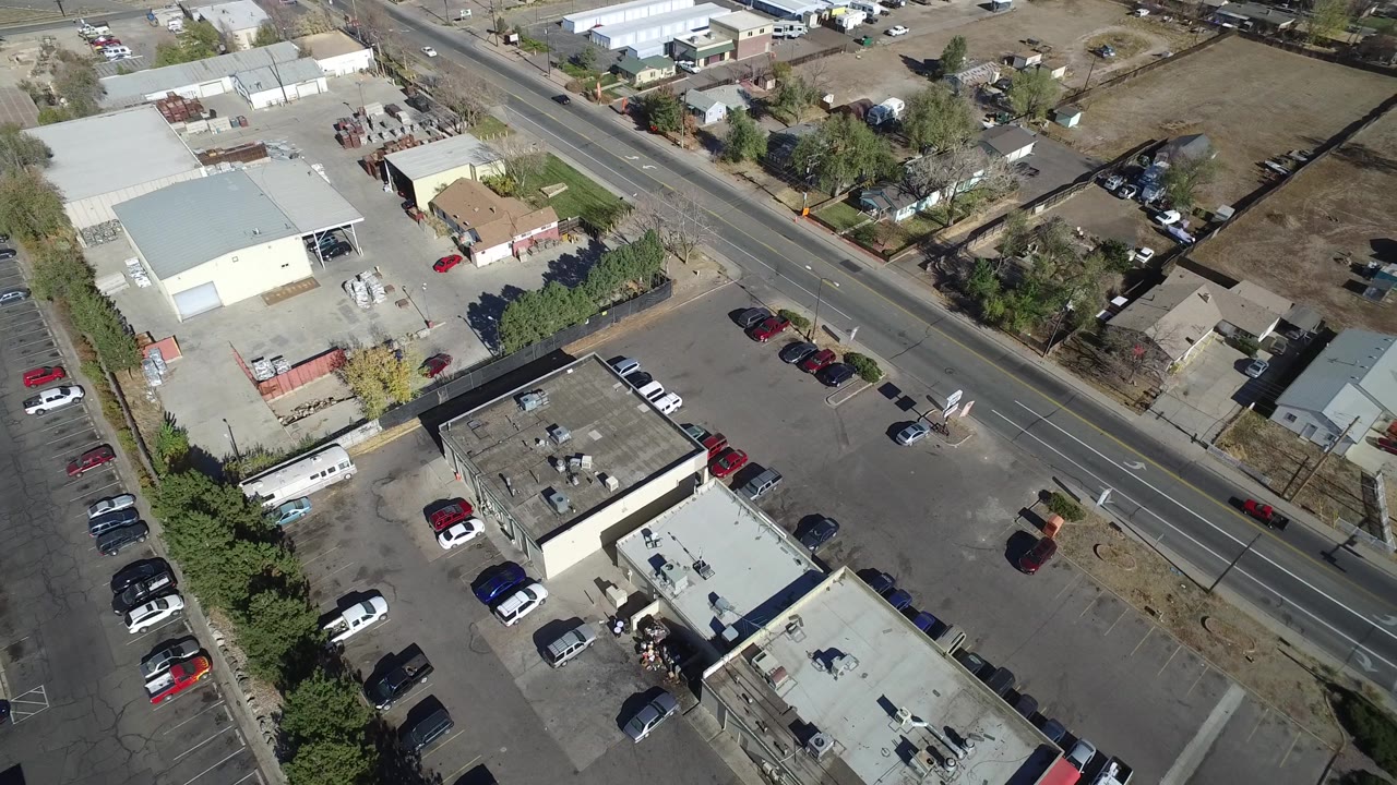 Second overhead frame in Westminster, Colorado, with commercial rooftops in the lower half, a road crossing the upper frame, nearby houses, parked cars, and no visible people.