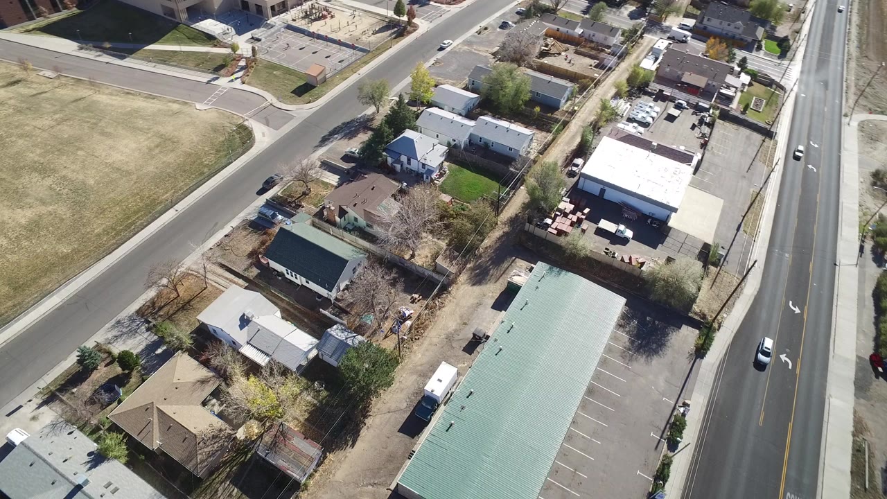 Aerial view of a suburban road beside houses and a long green-roofed building.