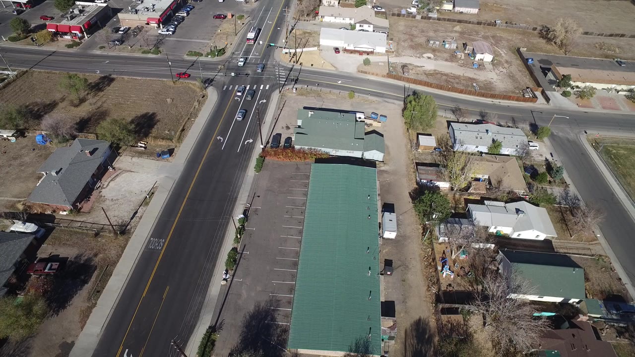Overhead view of a suburban intersection, green-roofed building, homes, and parked cars.