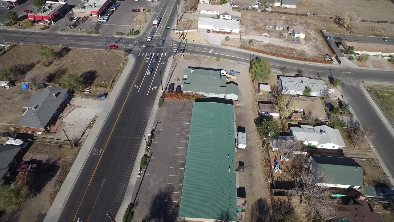 Overhead Westminster, Colorado view with the main road centered, a cross street at the top, small buildings, residential yards, leafless trees, vehicles, and no visible people.