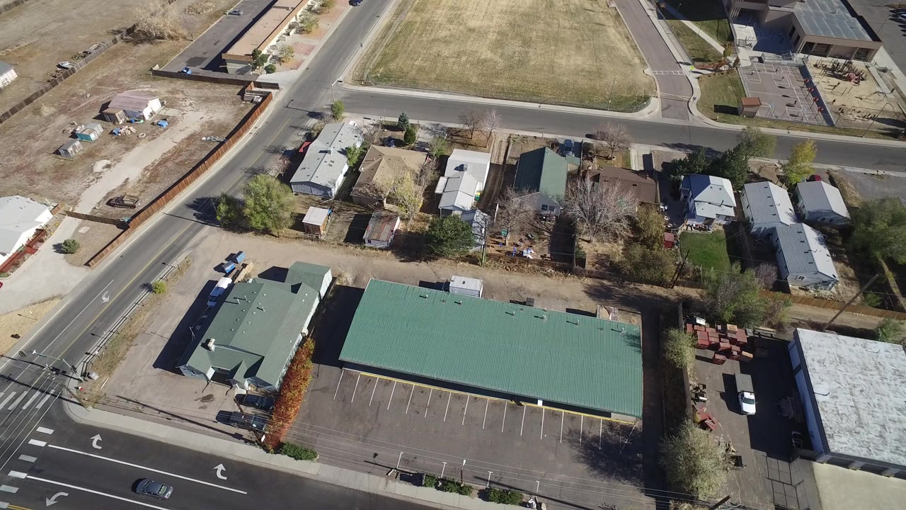 Overhead view of a green-roofed building, parking lot, roads, and nearby homes.