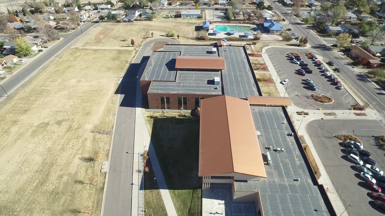 Overhead suburban view of a building complex, parking lot, roads, and houses.