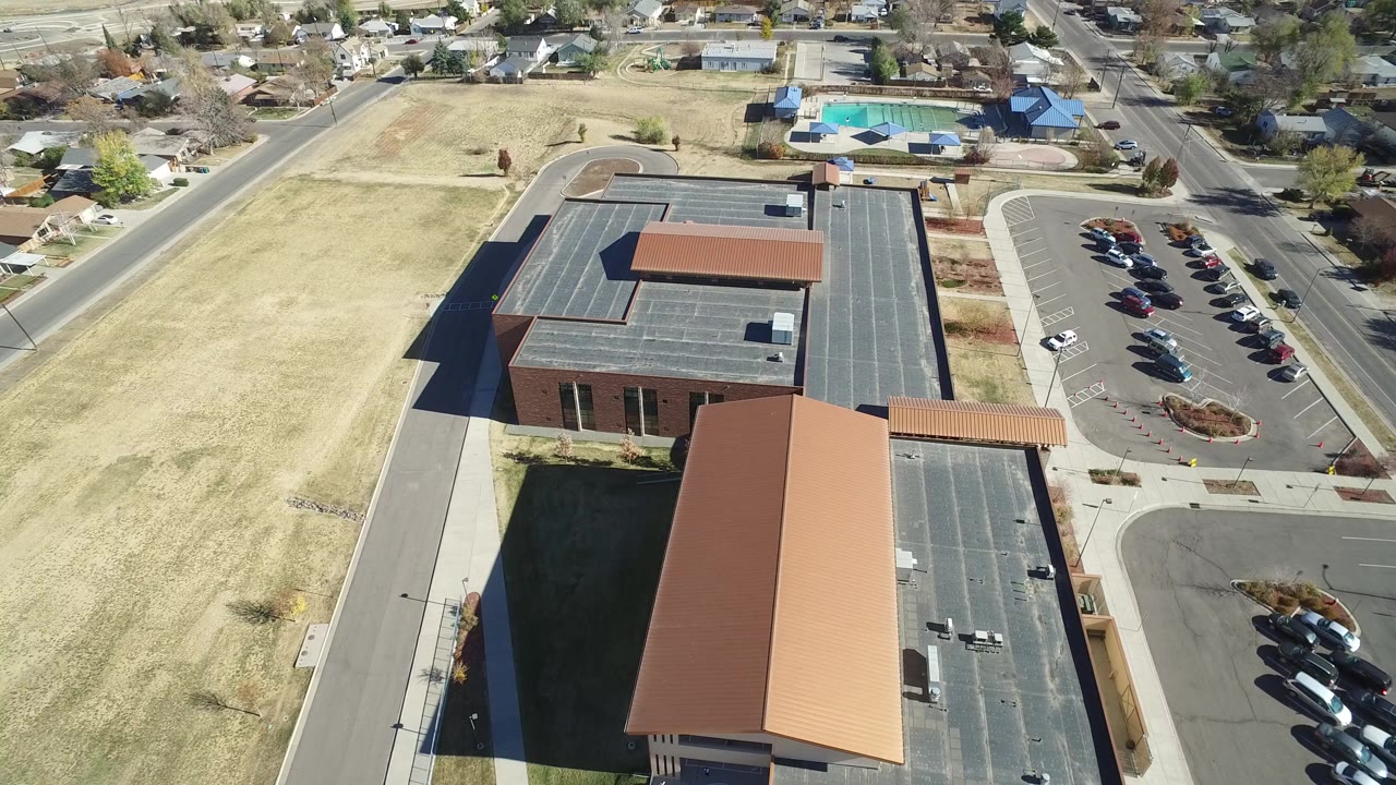 Aerial view of large buildings, parking lots, roads, grass fields, and nearby homes.