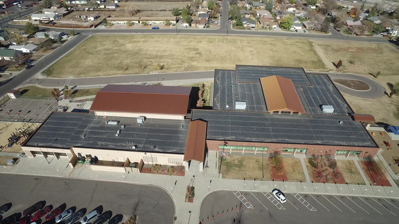 Aerial view of a large low-rise building with parking lots and homes beyond.