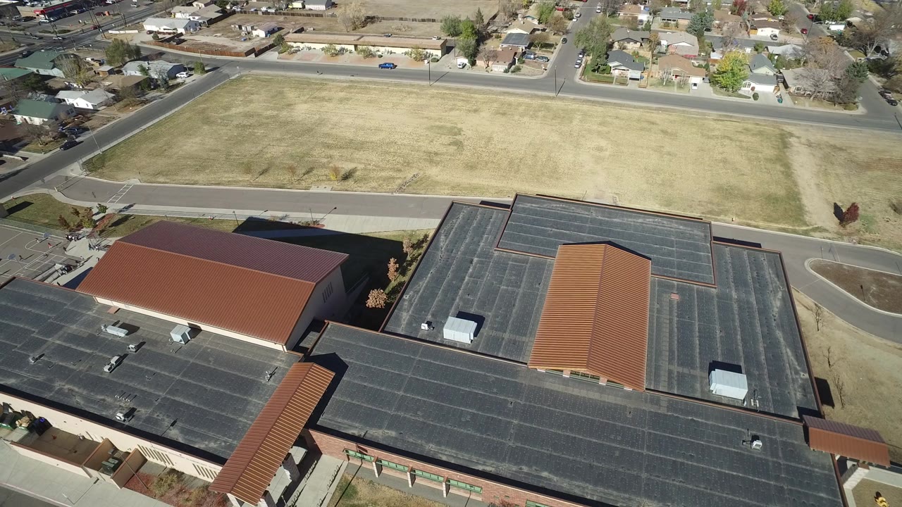 Bird's-eye view of flat rooftops, orange roof sections, road, field, and houses.