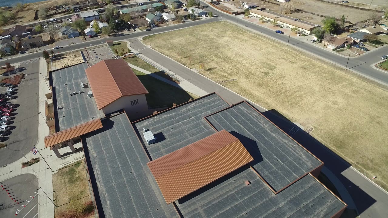 Aerial view of a large flat-roofed building beside a pale lawn and roads.