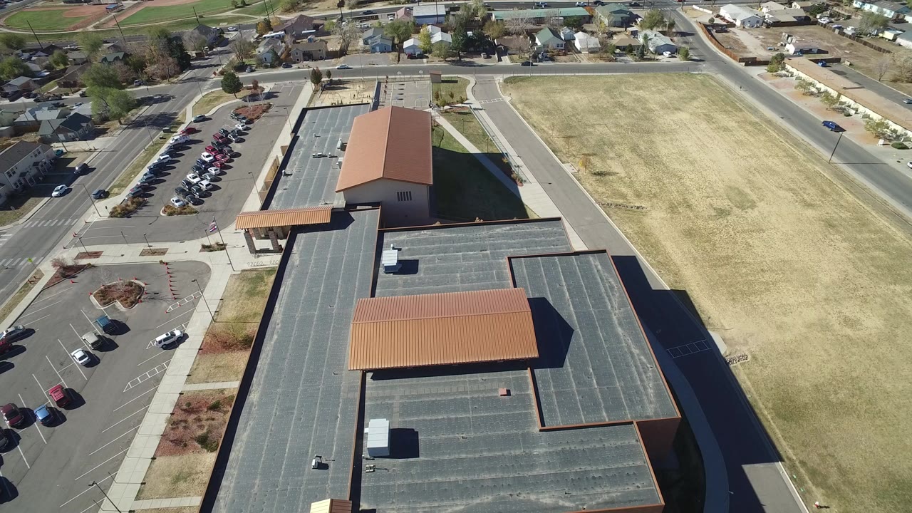 Aerial view of a large brick building, parking lot, roads, and grass field.