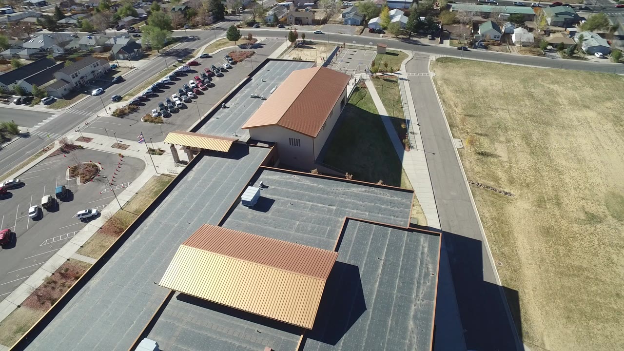 Aerial view of tan-roofed facility buildings beside roads and a large grass field.