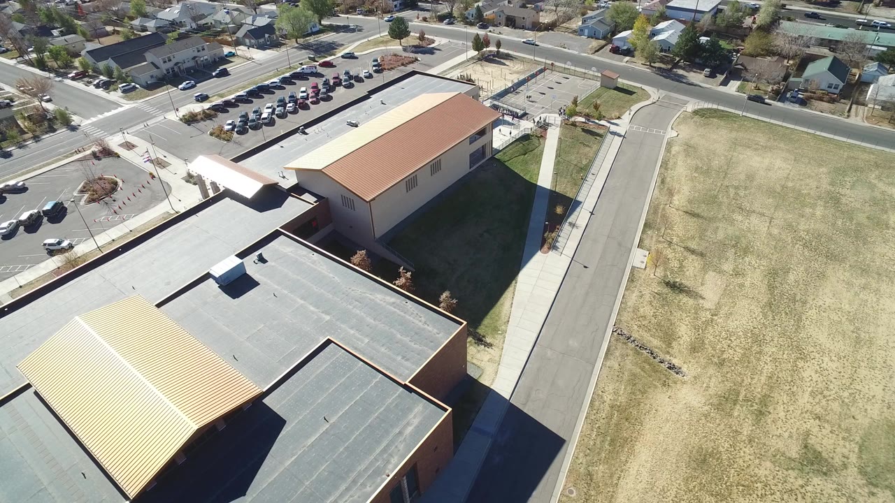 Aerial view of commercial roofs, road, grass field, parking, and homes.