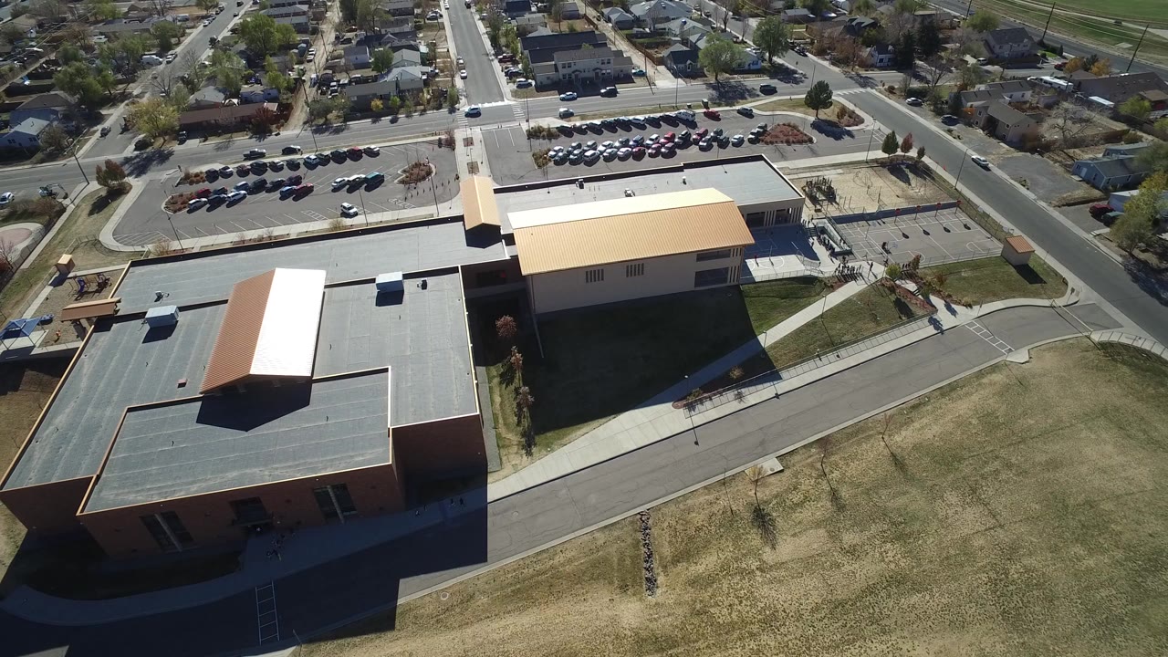 Aerial view over flat-roofed buildings, roads, parking, and nearby homes.