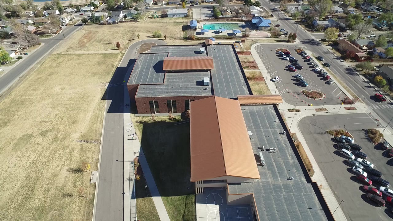 Aerial view of a commercial building, parking lot, roads, field, and neighborhood.