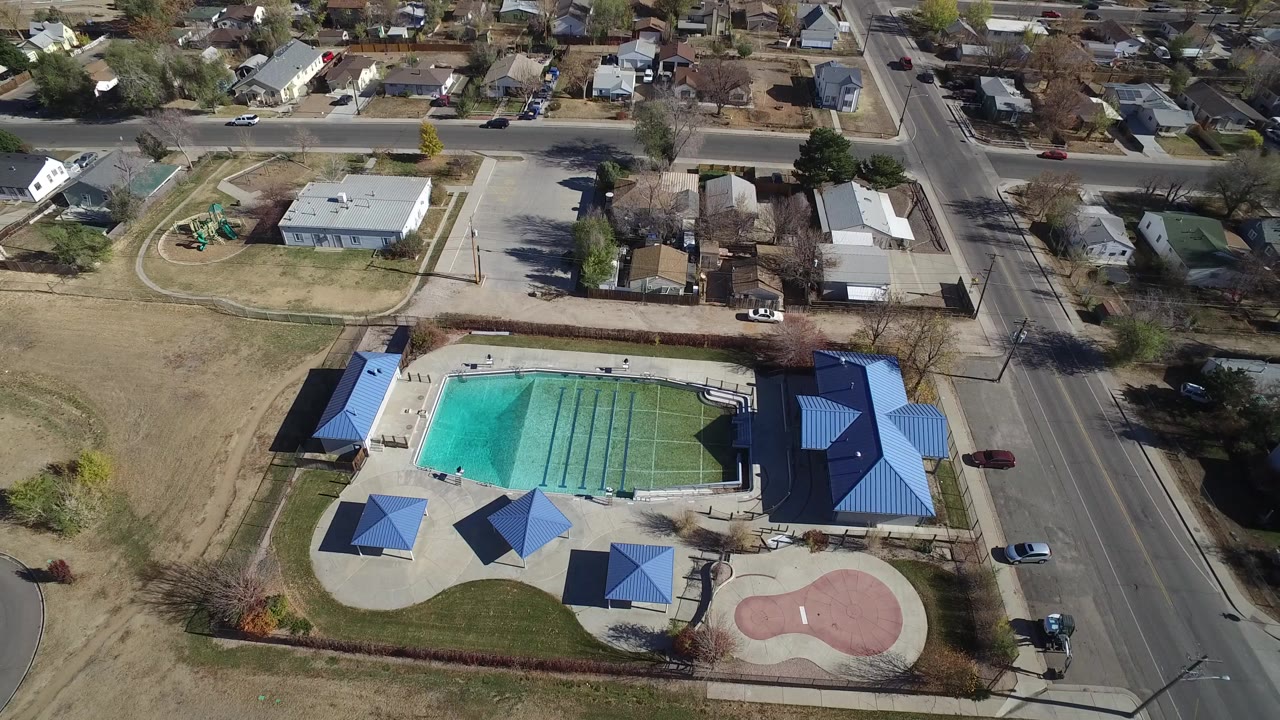 Aerial view of neighborhood pool, blue-roofed structures, road, and nearby houses.