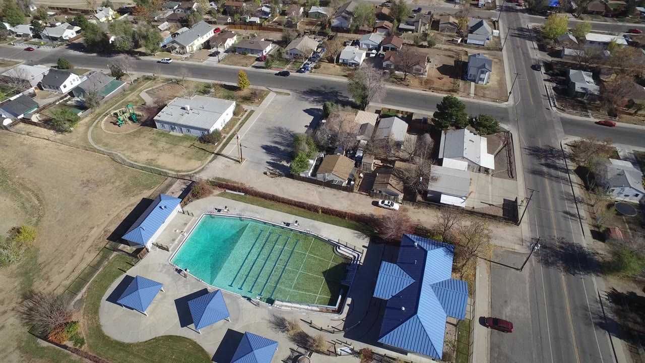 Aerial view of an outdoor pool beside blue-roofed park structures and neighborhood streets.