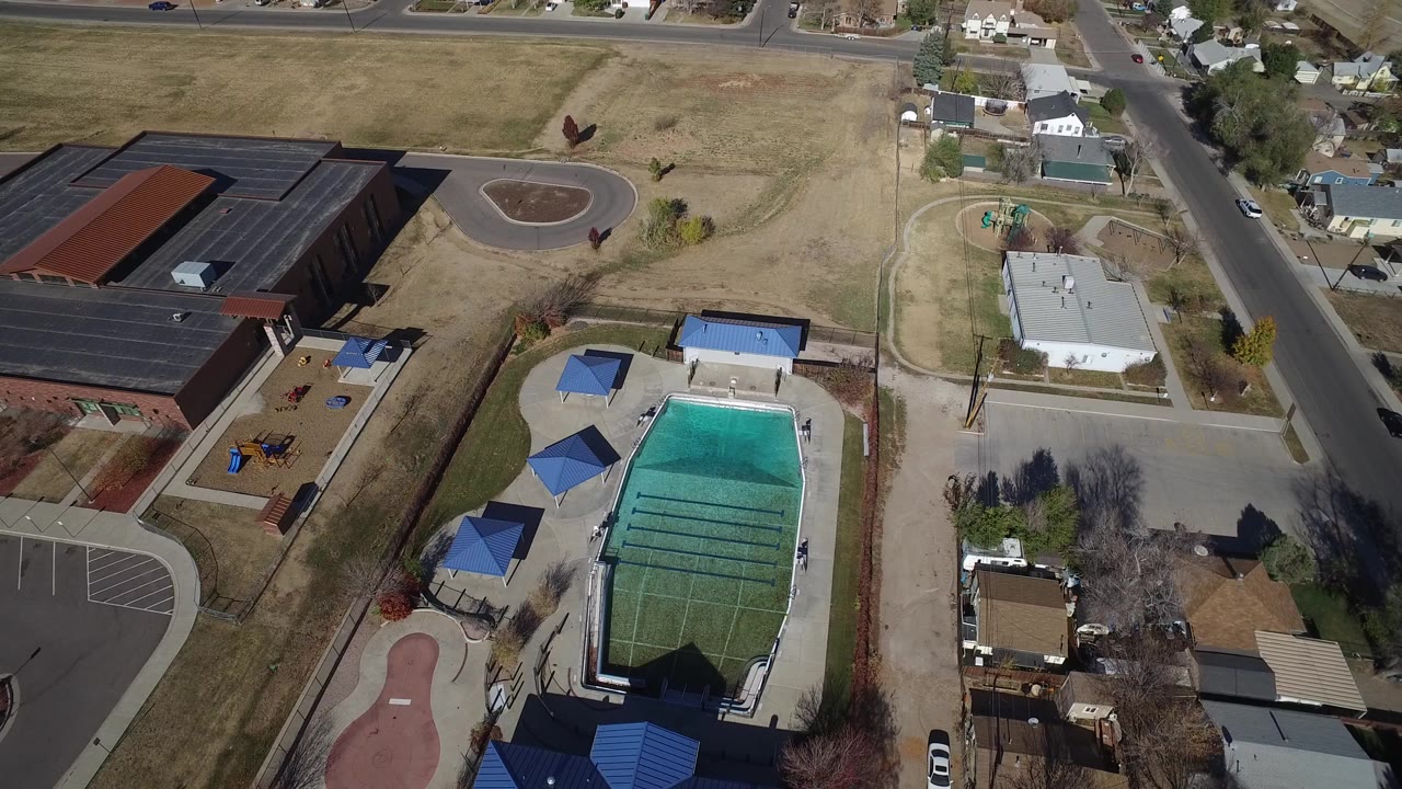 Aerial view of a pool, playground, brick building, roads, and houses.