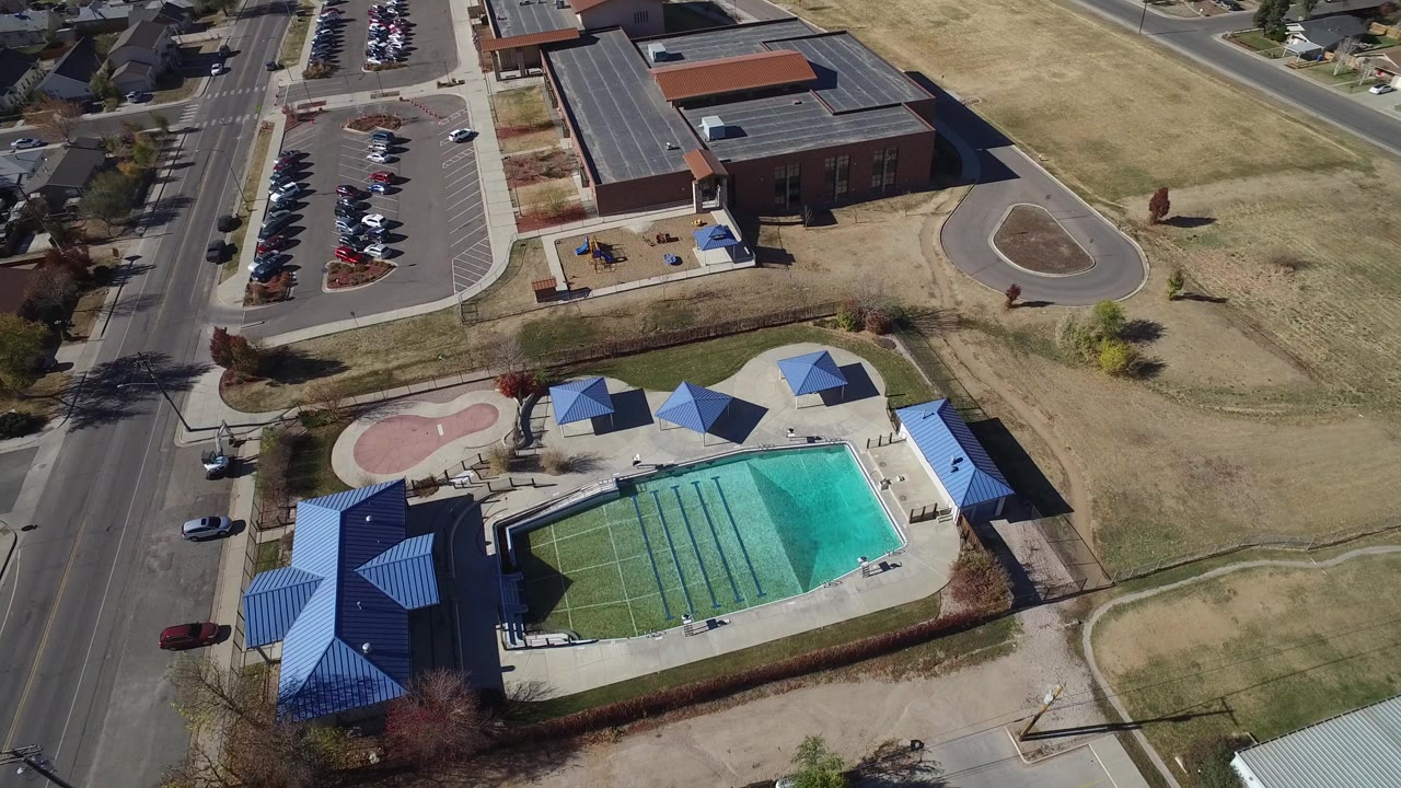 Aerial view of a pool complex with blue roofs, parking, roads, and dry grass.