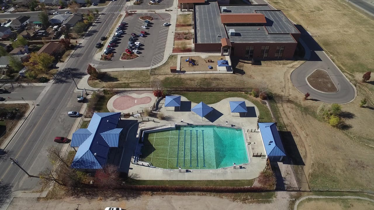 Aerial view of an outdoor pool complex beside a road and brick building.