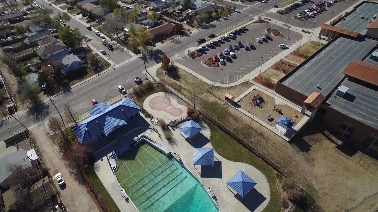 Aerial view of an outdoor pool beside roads, parking, houses, and blue shade structures.