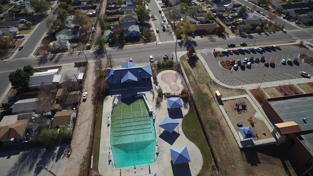 Aerial view of outdoor pool, blue roofs, parking lot, streets, and homes.