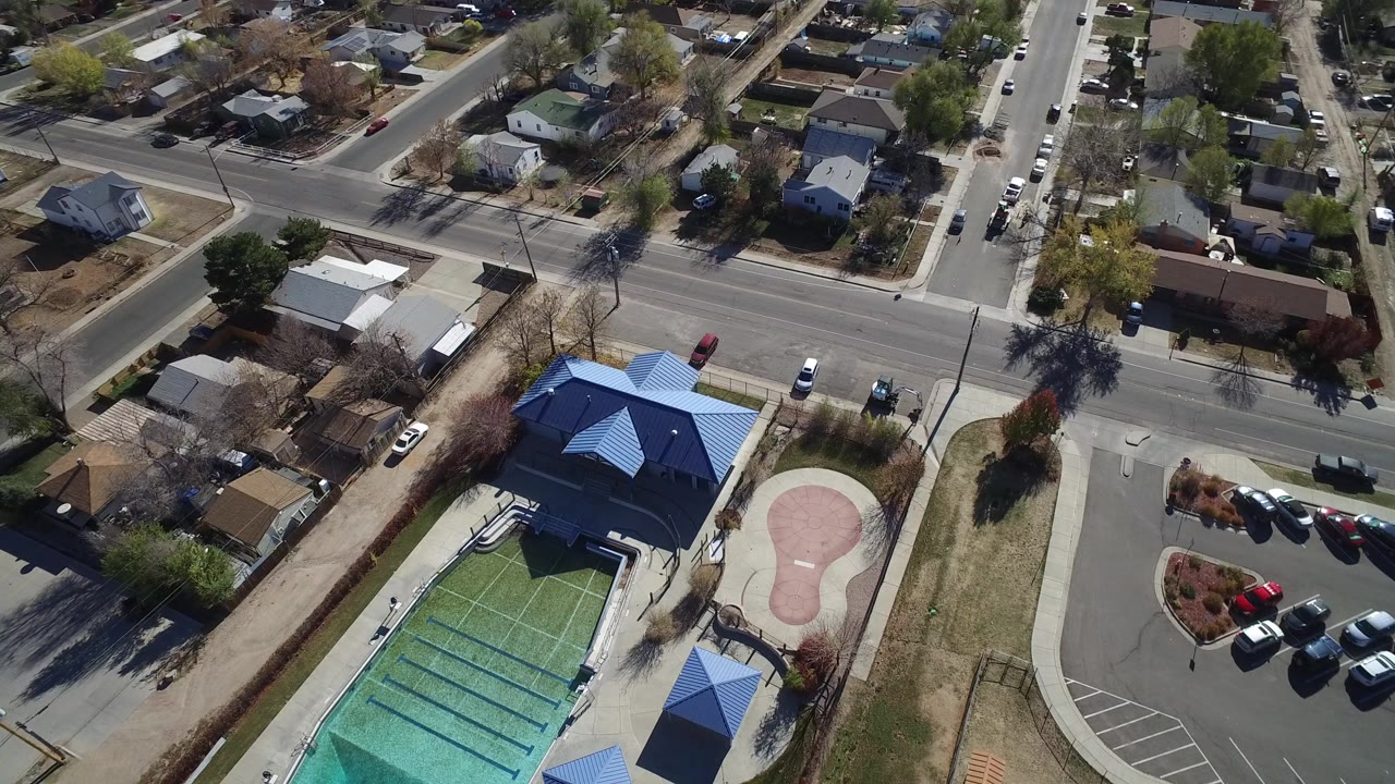 Aerial view of outdoor pool, mini-golf green, blue-roofed building, roads, and houses.