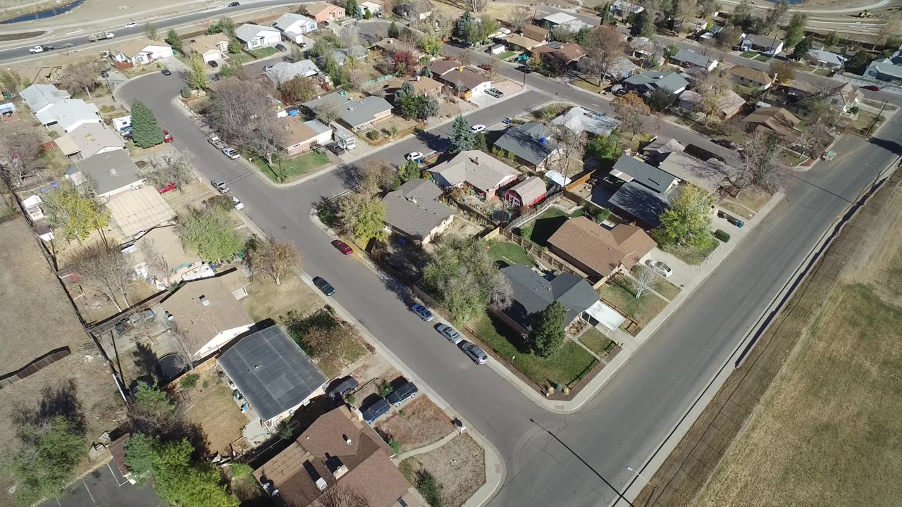 Aerial view of suburban houses, streets, trees, and an open grassy lot.
