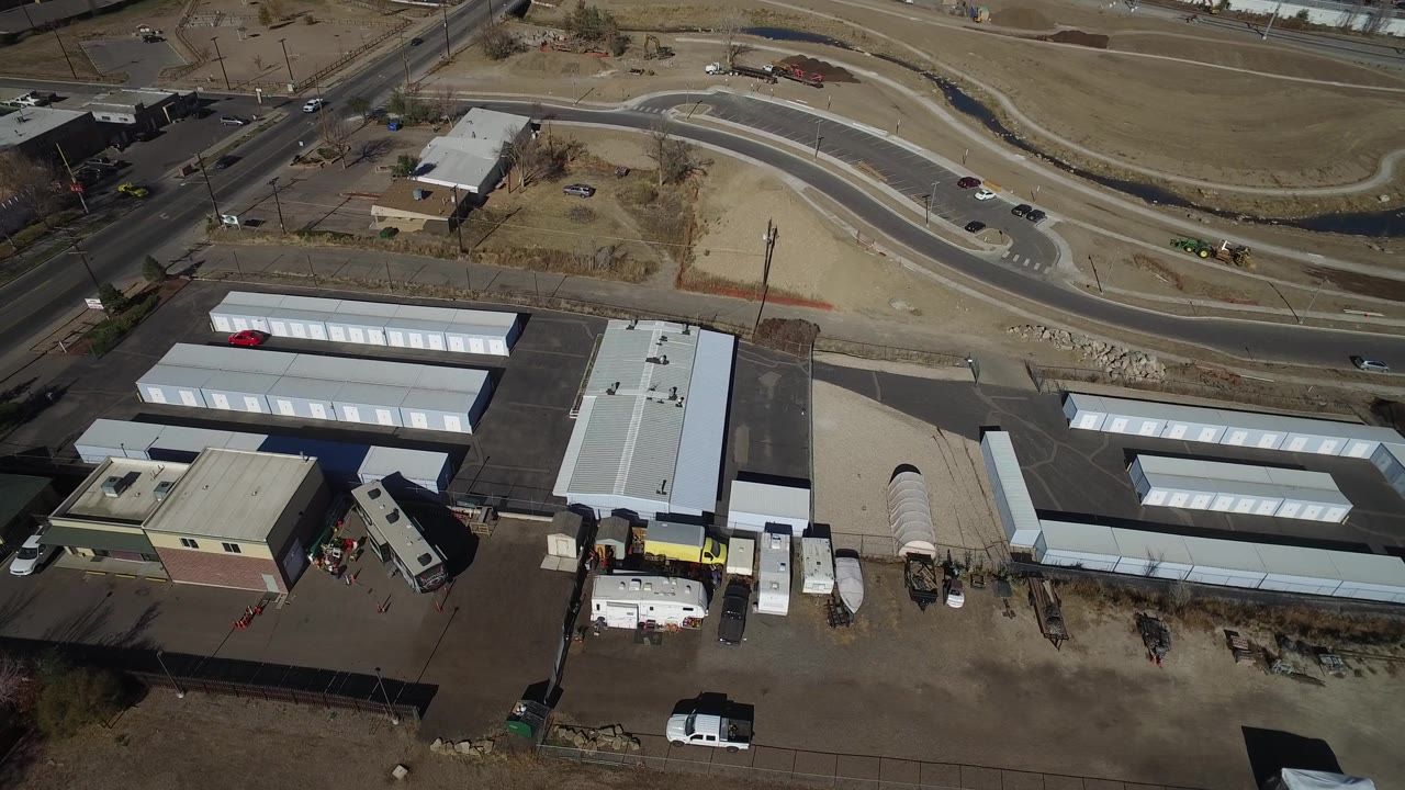 Drone view of storage units, industrial buildings, road, and drainage channel.