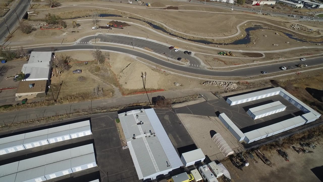Overhead Westminster, Colorado view with a winding drainage channel near the top, light industrial rooftops below, parked vehicles, and no visible people.