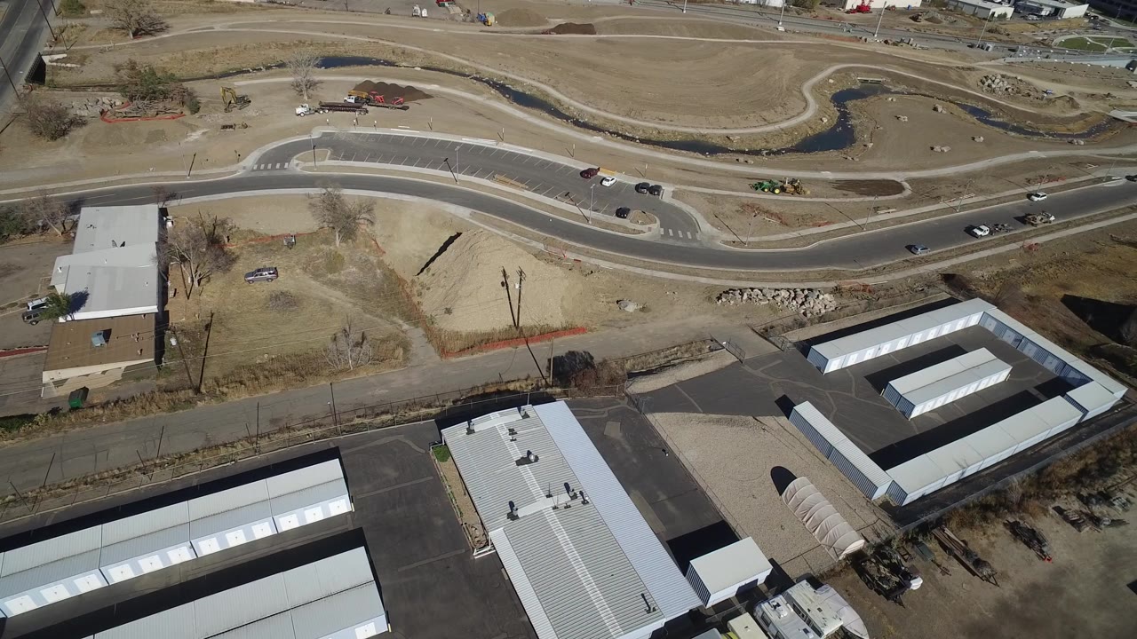 Aerial view of a road, dirt lots, storage units, and nearby buildings.