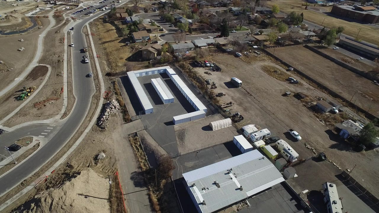 High aerial frame over an industrial property in Westminster, Colorado, with white roofs, paved yards, dirt lots, curved roads, nearby homes, and no visible people.