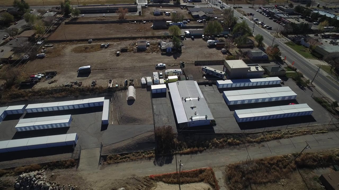 Aerial frame in Westminster, Colorado with long pale-roof storage rows, a central road edge, open dirt fields, scattered vehicles, and no visible people.