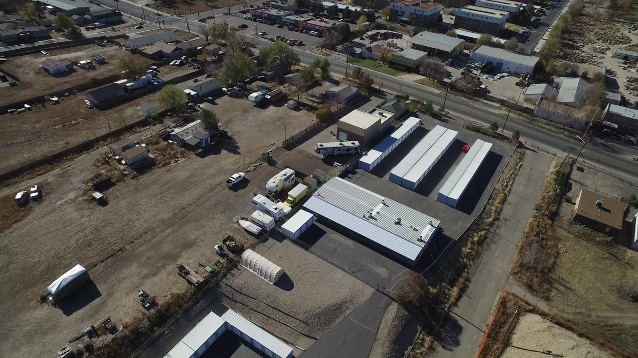 Overhead Westminster, Colorado view centered on light-roofed industrial buildings, parked trucks, open dirt ground, and no visible people.