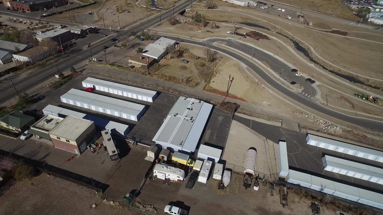 High aerial view over Westminster, Colorado storage sheds and industrial yards beside curving roads and dry open ground, with no visible people.