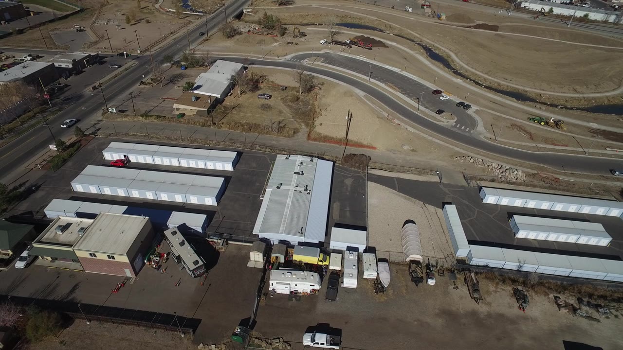 Aerial view in Westminster, Colorado showing white rectangular storage buildings, paved lots, a curved road, dry open ground, and no visible people at the start of the clip.