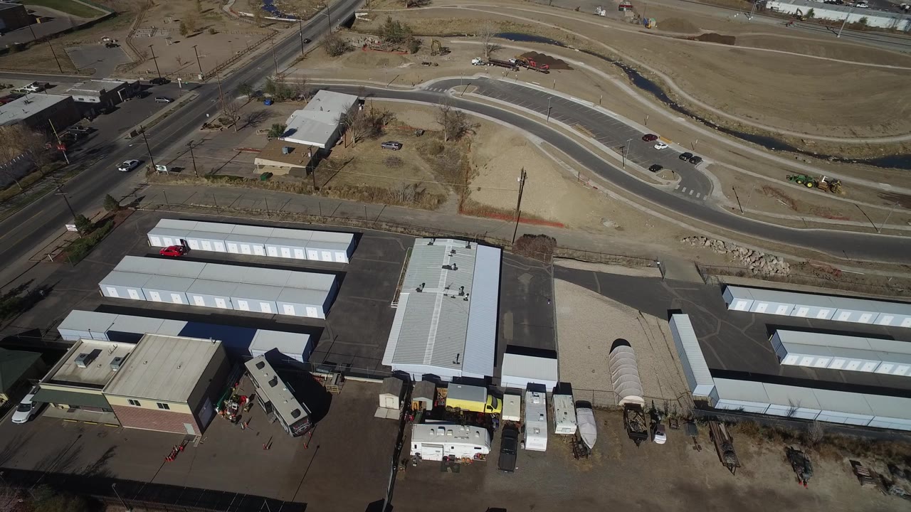 Aerial frame of storage units, parked vehicles, and curved roadway.